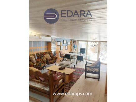 Interior view of a living room featuring a patterned sofa, wooden furniture, and a desk area.